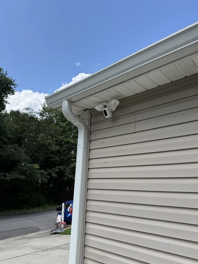 Floodlight camera mounted at the corner of a house under the eave by the gutter